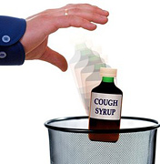 A Hand throwing a bottle of cough syrup into garbage can.
