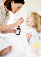 A mother giving her sick little girl some cough syrup.