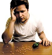 Man with a headache sitting at table with pain pills scattered over its surface.