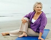 Elderly woman doing yoga on beach.